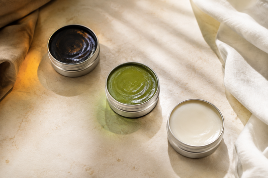 Three unbranded open Thai balm tins in black, green and white arranged on pale stone